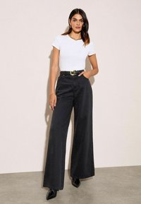 Fekete, bő szárú farmernadrág magas derékkal, ami egy testhez simuló fehér pólóval van párosítva. Az öltözethez egy láncnyaklánc és egy fekete öv tartozik.