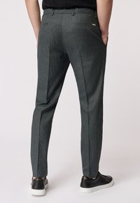 Pantaloni grigi a fantasia con vestibilità su misura, dotati di tasche e una texture liscia. Indossati con sneakers nere.