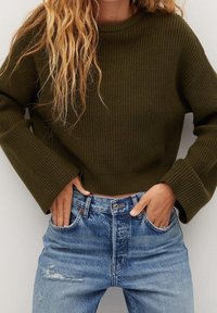 Olijfgroene ribbeltrui met brede mouwen, gecombineerd met lichtblauwe versleten denim jeans met een knoopsluiting en vijf zakken.