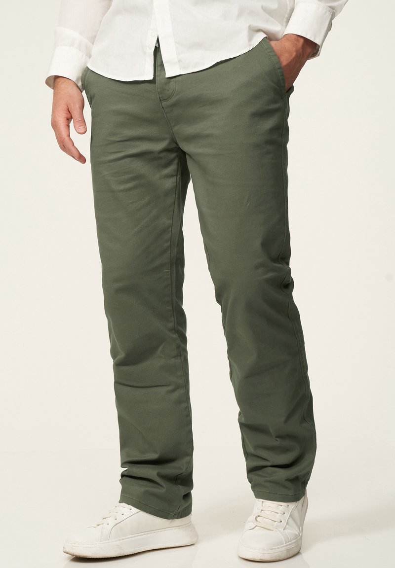 Green cotton blend trousers with a straight fit, featuring side pockets and a smooth texture, paired with white sneakers.