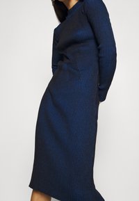 Stickad klänning med ribbad struktur i m örkblått med ljusblå ränder. Långa ärmar, knälång med en figurnära silhuett.