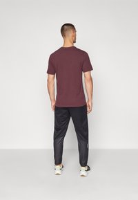 T-shirt bordô de manga curta combinada com calças de treino pretas com um design texturizado. Ténis desportivos em cores contrastantes.