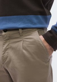 Βαμβακερό πουκάμισο με μακριά μανίκια, σχεδίαση με καφέ και μπλε ρίγες, συνδυασμένο με μπεζ παντελόνι με πλαϊνές τσέπες και υφή.