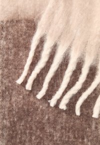 Sciarpa di lana in marrone e crema, caratterizzata da una texture morbida e una frangia attorcigliata lungo un bordo, che crea un aspetto stratificato.