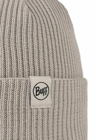 Gorra de punto gris claro con textura acanalada y un dobladillo. Presenta una etiqueta de tela de marca con la palabra "Buff" en un diseño circular.