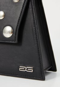 Sac en cuir noir avec de grands clous métalliques, présentant une forme triangulaire élégante et un logo argenté sur le côté.