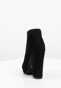 Botín de ante negro hasta el tobillo con punta redonda y un tacón alto y grueso. Presenta una textura suave y un diseño minimalista.