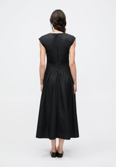 Fekete, térdig érő ruha vállkendővel, testhezálló felsőrésszel, rugalmas derékrésszel és bővülő szoknyával. Hátul cipzáras záródással.