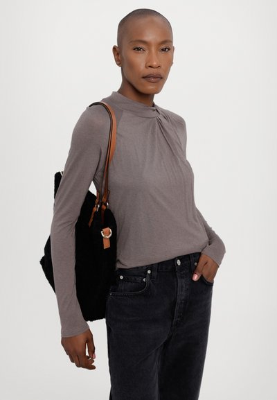 Langslavige, taupe top met een geraffineerde halslijn, gecombineerd met zwarte jeans en een zwarte tas met structuur die een bruine band heeft.