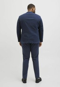 Dunkelblaues Sakko und Hose aus strukturiertem Stoff. Das Sakko hat ein schlankes Design mit einem Schlitz und schlanken Hosen. Schwarze Schuhe.