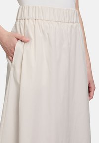 Spódnica z elastyczną talią w jasnym beżowym kolorze, o luźnym kroju i bocznymi kieszeniami, prezentująca gładką, miękką teksturę.