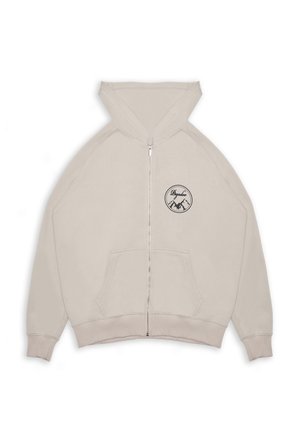 Beige zip-up hoodie with front pockets, attached hood, ribbed cuffs, and a round black mountain logo with text on the left chest.