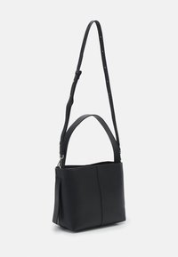 Sac à main en cuir noir au design structuré, doté d'une longue sangle réglable et d'une ouverture supérieure. Texture lisse et détails de couture minimaux.