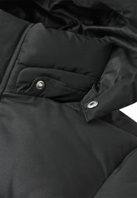 Schwarze gepolsterte Jacke im Nahaufnahme, die eine gestickte Tasche mit Druckknopf und einen gesteppten Kragen mit silbernem Druckverschluss zeigt.