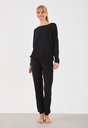 T-shirt noir à manches longues avec un large col et une coupe décontractée, associé à un pantalon noir fuselé avec des poignets et une ceinture élastiques.