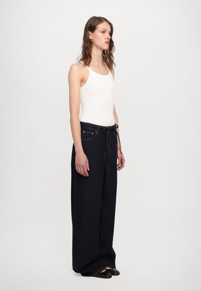 Mørke denim vide bukser med snoretræk i taljen, parret med en tætsiddende hvid tanktop. Glat tekstur, minimalistisk design.