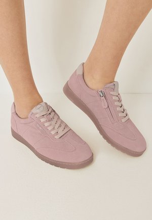 Por poros rózsaszín velúr sneaker cipő fűzőkkel és oldalsó cipzárokkal, mezítláb viselve, fehér háttér előtt.