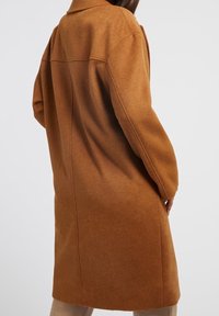 Bruine wollen mixjas met een relaxte pasvorm, een oversized kraag en lange mouwen. Naaddetails lopen over de rug. Glad textuur.