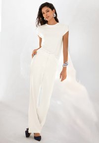 Witte t-shirt met korte mouwen gecombineerd met brede witte broeken en marineblauwe blokhak schoenen. Accessoires omvatten een blauwe armband en oorbellen met een ring.