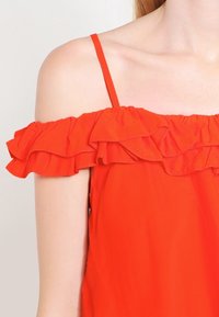 Röd off-shoulder topp med volangdetaljer vid halslinningen, tunna axelband och en mjuk tygkänsla.