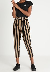 Czarna koszulka z logo, zestawiona z wysokimi beżowo-czarnymi spodniami w paski z przewiązanym paskiem. Całość dopełniają czarne sneakersy.