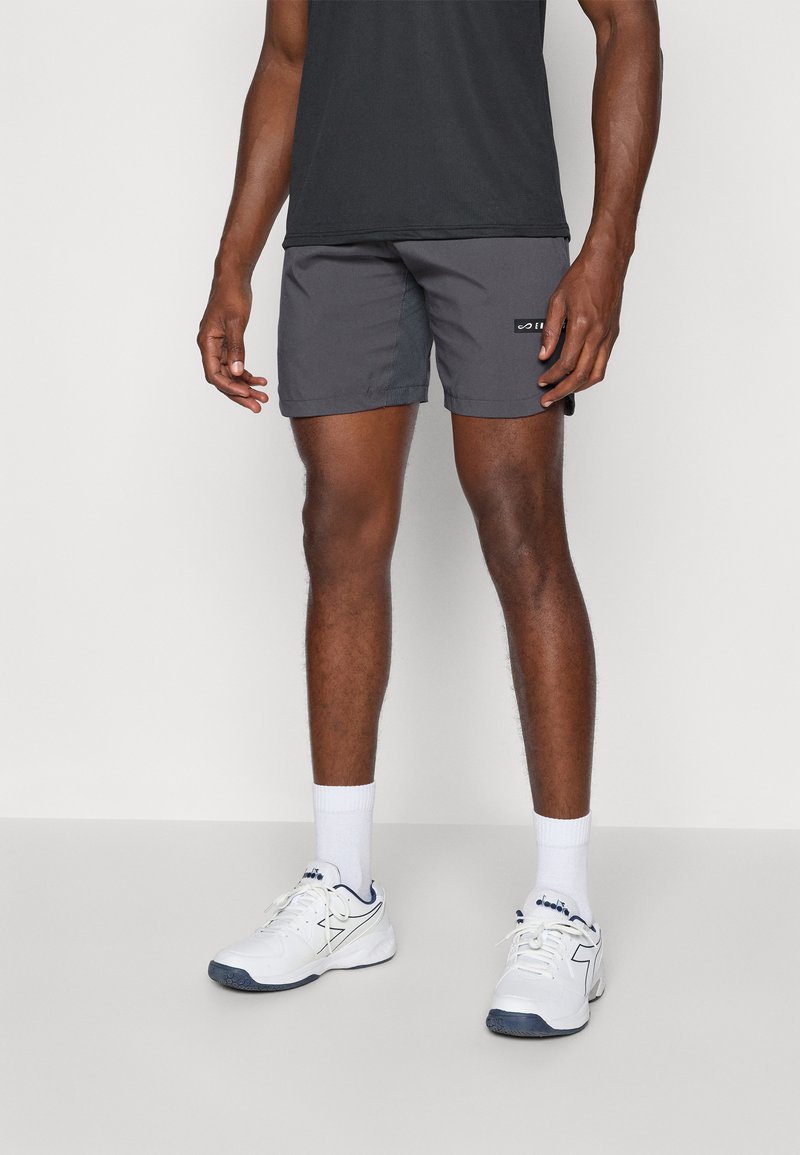 Shorts de sport gris en matière légère, dotés d'une poche latérale et d'un petit logo sur l'ourlet, portés avec des chaussettes de sport blanches et des chaussures.