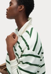 Grön och vit randig sweatshirt med ribbad krage, tillverkad av mjukt bomullsmaterial och synliga sömmar längs axlarna och ärmarna.