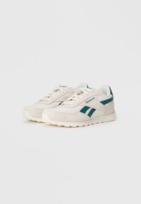 Un paio di sneakers Reebok bianche e teal con lacci, suola testurizzata e dettagli in suede su uno sfondo bianco semplice.