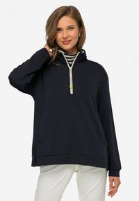 Sudadera con capucha de color navy, con cuello interior a rayas, cremallera de cuarto, bolsillos laterales, corte relajado y textura suave. Detalles con un tirador de cremallera verde.