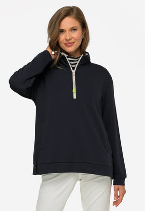 Felpa con cappuccio blu marino, colletto interno a righe, zip a quarto di lunghezza, tasche laterali, vestibilità rilassata e texture morbida. Accentuata da una zip verde.