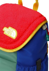 Krāsaina mugursoma ar sarkanu vilnas pārsegu, dzeltenu apmali, zilām un zaļām detaļām un The North Face logotipu. Ietver regulējamu aparatūru.