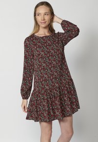 Blumenkleid mit langen Ärmeln, schwarzem Grund, rotem und weißem Blumenmuster. Mit einem gestuften Rock und einem runden Ausschnitt.