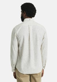 Chemise à manches longues, à boutons, de couleur blanc cassé avec un motif noir moucheté. Dispose d'un col classique et d'un pli dans le dos pour plus de liberté de mouvement.