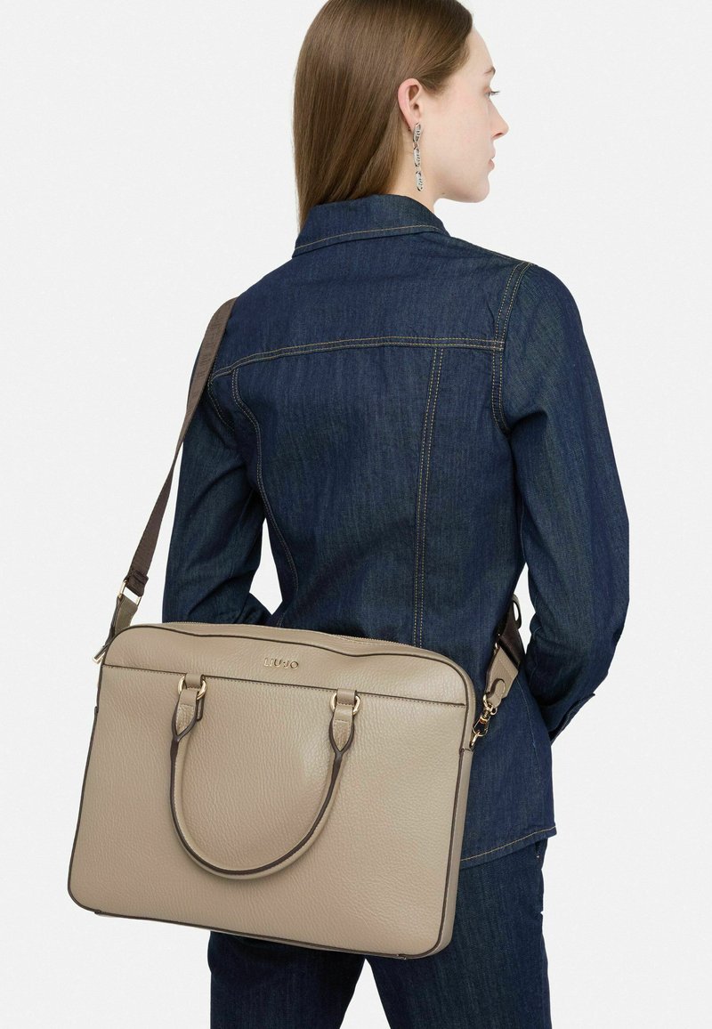 Beige leren laptoptas met dubbele bovenhandvatten en een verstelbare schouderband, met een gladde textuur en gouden accenten.