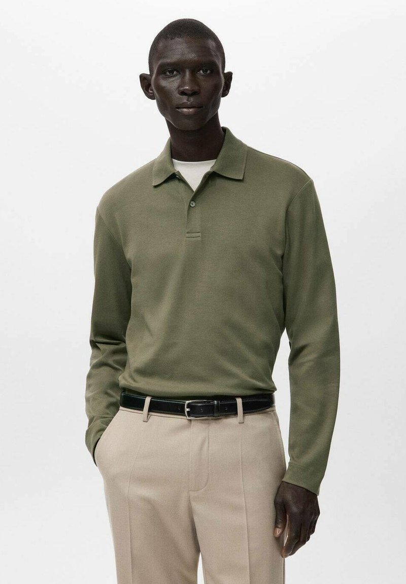 Olivegrünes Poloshirt mit langen Ärmeln und Kragen, mit einer Knopfleiste. Kombiniert mit beigen Hosen und einem schwarzen Gürtel.