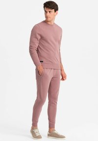Staubige rosa Sweatshirt und passende Jogginghose aus einem weichen Stoff. Mit ribbelten Bündchen und Taillenbund, seitlichen Taschen und einem schwarzen Akzent-Tag.