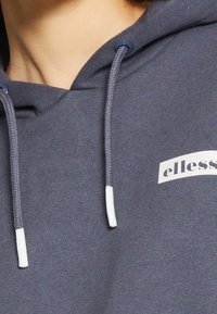 Sweat à capuche gris en tissu doux, avec un logo blanc et des cordons de serrage contrastants. Design simple avec une coupe décontractée et sans motifs.