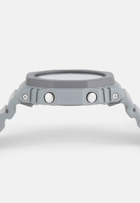 Gray rubber watch with a round face, two white buttons on the side, and a textured strap for grip. Simple, sporty design.