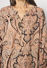 Langærmet skjorte i sort med et detaljeret paisley-mønster i nuancer af pink og orange. Har en V-halsudskæring og små knaplukninger.