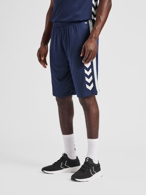 Mann trägt marineblaue Sportshorts mit weißen Chevron-Streifen, weiße Sportsocken und schwarze Laufschuhe mit weißen Sohlen.
