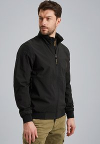 Schwarze Bomberjacke mit hohem Kragen, Reißverschluss vorn und elastischen Bündchen. Verfügt über seitliche Taschen mit Reißverschluss und eine glatte, matte Textur.