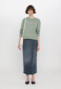 Zelená mikina s logem "ARMANI EXCHANGE", spárovaná s tmavými džínovými sukněmi po kotníky. Nabízí elegantní design a jemnou texturu.