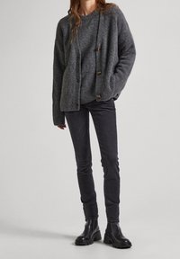 Šedý vlněný kardigan s volným střihem, který má tři knoflíky a žebrovaný lem, v kombinaci se slim černými džíny a černými kotníkovými botami.