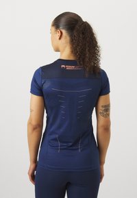 Camiseta atlética de manga curta, azul marinho, com painéis em malha e design perfurado nas costas. Apresenta um logótipo laranja na gola.