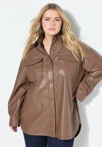 Camicia oversize in finta pelle marrone con due tasche sul petto, maniche lunghe e orlo arrotondato. Texture liscia e finitura lucida.