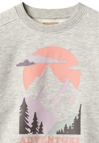 Sweatshirt gris clair présentant un paysage de montagne avec des pins, un soleil rose, et le mot « AVENTURE » en lettres roses.