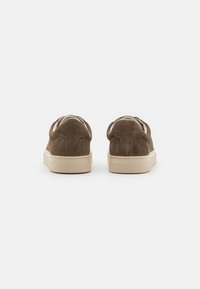 Brune semskesneakers med lavt snitt, utstyrt med en beige gummisåle og minimal merkevare. Glatt tekstur og avrundet hæl.