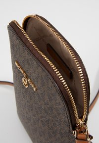 Brun canvas crossbody-väska med guldblixtlås, med en strukturerad utsida och logotypdetaljer. Fodrad inredning med kortfack.