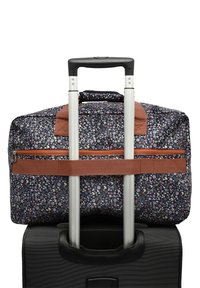 Rollkoffer mit einem schwarzen strukturierten Körper und einer blumengemusterten Reisetasche oben, gesichert mit einem braunen Gurt. Silberner ausziehbarer Griff.
