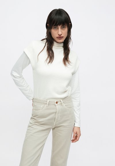 Λευκό ριμπ μπλουζάκι με ψεύτικο λαιμό, φορεμένο πάνω από ένα λευκό πουκάμισο μακριών μανικιών, σε συνδυασμό με μπεζ παντελόνι κανονικής γραμμής και καφέ διακοσμητικό κουμπί.